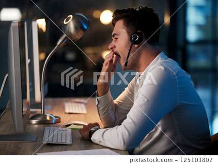 Tired, yawn and call center man in office at night for telemarketing, customer service and crm consulting. Exhausted, sleepy and overworked young call centre salesman with burnout and fatigue at desk 125101802