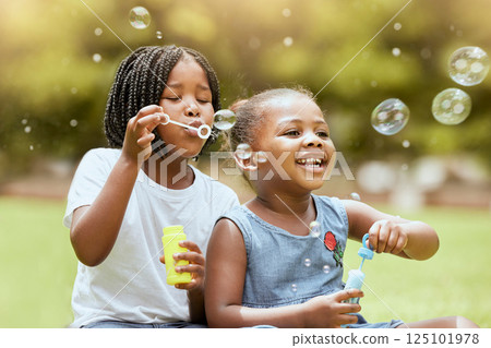 Black kids, children and blowing bubbles at park, having fun and bonding. Girls, happy sisters and playing with soap bubble toys, relax and enjoying garden together outdoors in nature on grass 125101978