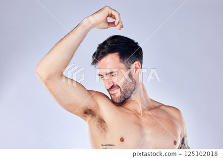 Armpit, stink and hygiene with a man model smelling his underarm in studio on a gray background for a deodorant product. Body, natural and sweat with a handsome young male sniffing his sweaty arm 125102018