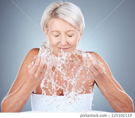 Water, splash and senior woman in studio for natural, cosmetic and facial routine for hygiene. Health, wellness and elderly lady doing clean, organic and beauty skincare treatment by gray background. 125102119