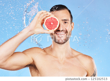Portrait, water splash and skincare with a handsome young male posing for natural body care. Shower, water and grapefruit with a man model in studio on a blue background for hygiene or hydration. Portrait, water splash and skincare with a handsome young male posing for natural body care. Shower, water and grapefruit with a man model in studio on a blue background for hygiene or hydration. 125102513