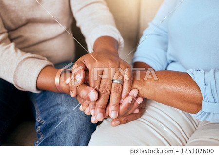 Support, love and closeup of people holding hands for comfort while sitting on a sofa together. Compassion, sympathy and friends praying, bonding and healing together in the living room of a house. 125102600