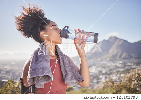 Music, workout and woman drinking water after exercise at sunrise along mountain, wellness and training on blue sky. Radio, water and black woman stop for break from fitness, running and cardio run 125102798