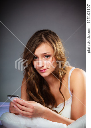 Woman on bed holding mobile phone. 125103107