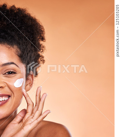 Skincare, beauty and black woman with facial cream on orange background studio for wellness. Makeup, cosmetics and half face of girl apply lotion, sunscreen and skincare products for dermatology care 125103205