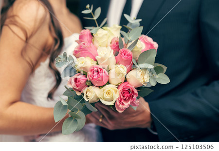 Flowers, wedding and love with a bouquet in the hands of a bride and groom on their marriage day closeup. Rose, married and celebration event with a floral arrangement in hand during a ceremony 125103506