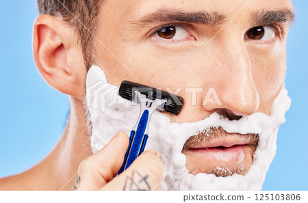 Grooming, cream and man shaving his face with a razor for wellness, skincare and health against a blue studio background. Beauty, young and portrait of a model with foam on beard for hygiene 125103806