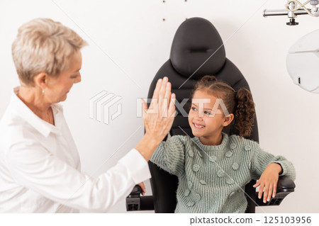 High five, optometrist and children with a girl and woman in an optometry appointment for prescription lenses. Motivation, eye test and success with a female child and optician in celebration High five, optometrist and children with a girl and woman in an optometry appointment for prescription lenses. Motivation, eye test and success with a female child and optician in celebration 125103956