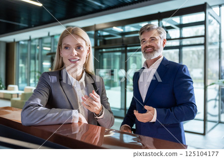 Businesswoman and her partner talking at receptionist desk in lobby 125104177