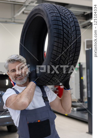 Man in service shop wearing uniform performing manual job to change tyres 125104334