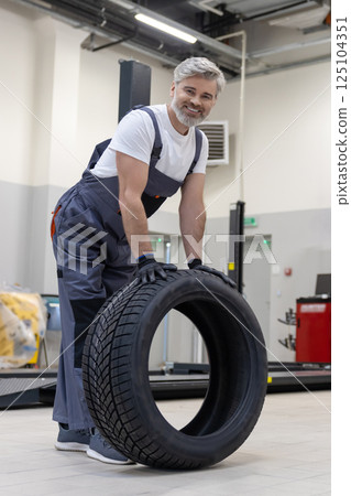 Mechanic holding tire tire at repair garage doing replacement of tires Mechanic holding tire tire at repair garage doing replacement of tires 125104351