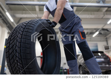 Unrecognizable automotive technician in garage checking wheel and fixing tire ensuring vehicle safety 125104369