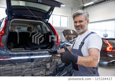 Male mechanic in uniform using tool in garage checking automobile for repair Male mechanic in uniform using tool in garage checking automobile for repair 125104417
