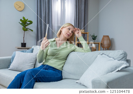 50 year old woman sitting with a fan in hand and suffering from heat 125104478