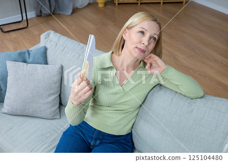 50 year old woman sitting with a fan in hand and suffering from heat 125104480