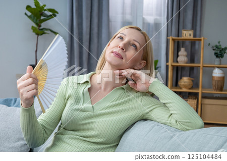 50 year old woman sitting with a fan in hand and suffering from heat 125104484