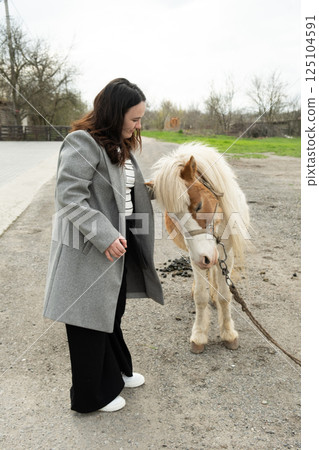 Woman stroking pet cute pony, friendship of people and animals Woman stroking pet cute pony, friendship of people and animals 125104591