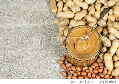 Peanut butter in a jar among scattered peanuts, space for text. Peanut butter in a jar among scattered peanuts, space for text. 125104603