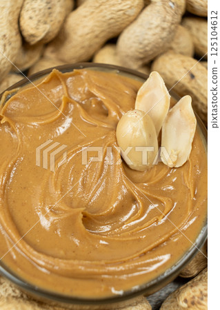 Peanut butter in a bowl among scattered peanuts 125104612