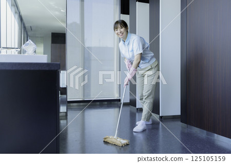 一名年輕的女清潔工正在擦拭辦公大樓衛生間的地板。照片提供：東京電子專門學校、電波學園 125105159