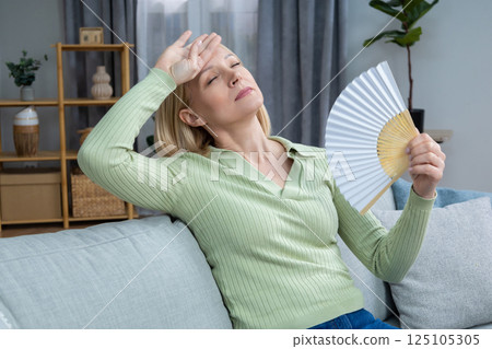 50 year old woman sitting with a fan in hand and suffering from heat 125105305