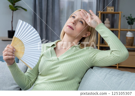 50 year old woman sitting with a fan in hand and suffering from heat 125105307