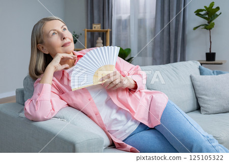 Smiling mid aged woman sitting on the sofa with a fan in hands 125105322