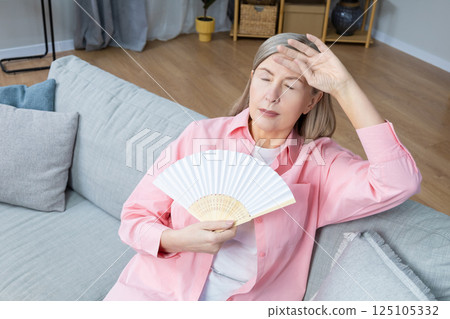 Mid aged woman in pink shirt with a fan in hands 125105332
