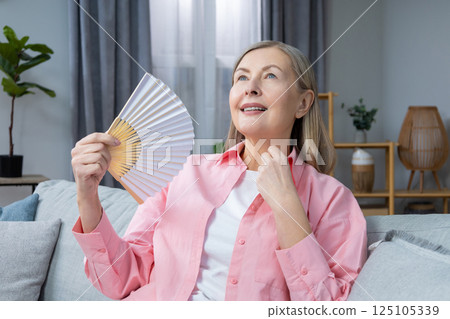 Mid aged woman in pink shirt with a fan in hands 125105339