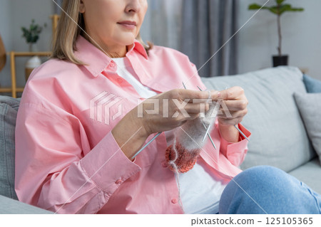 Woman in pink shirt sitting on the sofa and knitting Woman in pink shirt sitting on the sofa and knitting 125105365