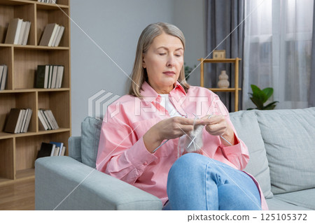Woman in pink shirt sitting on the sofa and knitting 125105372