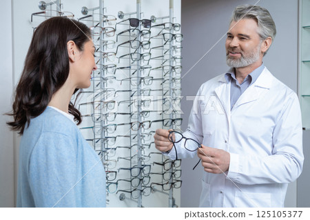 Woman choosing eyeglasses in optical store with oculist checking eyesight for vision care 125105377