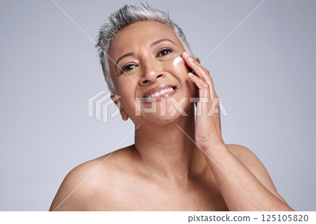 Face, skincare and beauty with a mature woman using moisturizer for antiaging treatment in studio on a gray background. Wellness, facial and portrait with a senior female inside for dermatology care 125105820