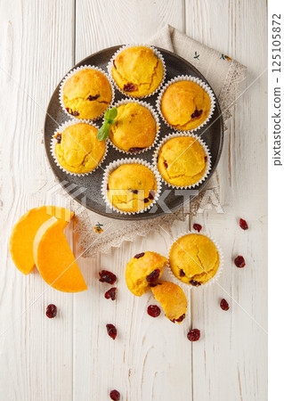 Tender muffins with pumpkin puree and cranberries close-up in a plate. Vertical top view 125105872