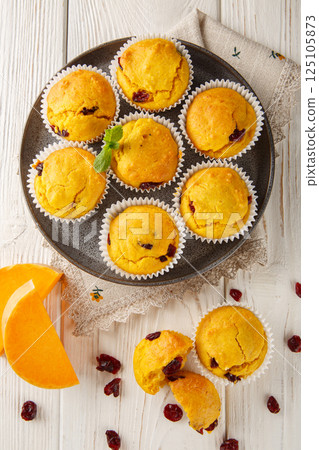 Soft and fluffy muffins flavored with pumpkin, cranberries, warm spices, and a touch of orange closeup on the plate. Vertical top view 125105873
