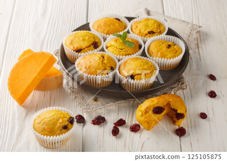 Freshly baked pumpkin muffins with dried cranberries, orange zest and spices close-up in a plate. Horizontal 125105875