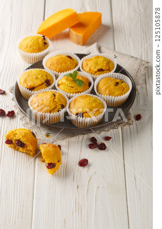Delicious pumpkin cranberry muffins are made with pumpkin puree and dried cranberries closeup on the plate. Vertical 125105878