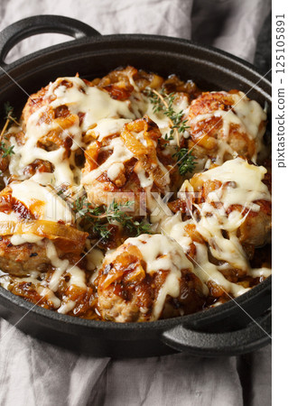 French onion meatballs smothered in rich caramelized onion gravy and topped with melty Gruyere cheese closeup on the pan. Vertical 125105891