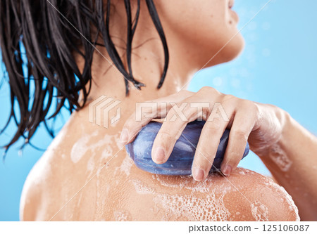 Hand, soap and shower with a woman cleaning her shoulder in studio on a blue background for hygiene. Water, bathroom and skincare with a female washing her skin for wellness or luxury treatment 125106087