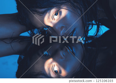 Face, beauty and reflection with a model woman in studio on a blue background against a mirror for skincare. Luxury, art and creative with an attractive young female mirrored in glass for wellness Face, beauty and reflection with a model woman in studio on a blue background against a mirror for skincare. Luxury, art and creative with an attractive young female mirrored in glass for wellness 125106103