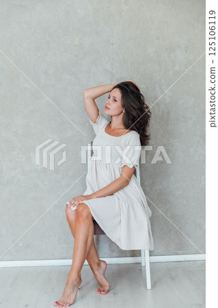 Portrait of a beautiful brunette woman in a light summer dress on a light background Portrait of a beautiful brunette woman in a light summer dress on a light background 125106119