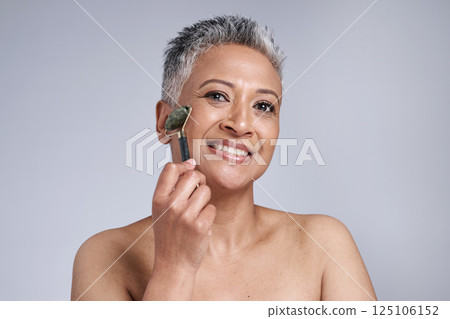 Black woman, beauty and skincare with a facial roller or rose quartz in studio for cosmetics or dermatology product on grey background. Face portrait of a senior model with a smile for wellness glow Black woman, beauty and skincare with a facial roller or rose quartz in studio for cosmetics or dermatology product on grey background. Face portrait of a senior model with a smile for wellness glow 125106152