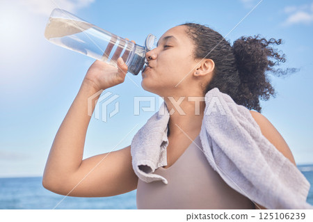 Water, fitness and woman with a drink after exercise, workout or training by the sea. Sports, motivation and energy from a runner with a bottle for hydration after running by the beach in nature 125106239