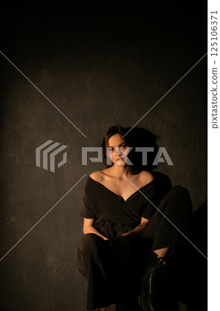 Beautiful woman in dark dress sitting on chair 125106371
