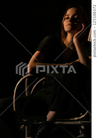 Beautiful woman in dark dress sitting on chair 125106372