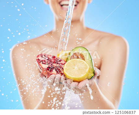 Water, hands and woman with fruit in studio on blue background for nutrition, wellness and health. Girl washing, cleaning and rinse fruits and vegetable for natural, fresh and organic ingredients 125106837