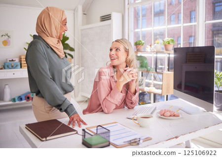 Business people, office and women talking at desk, chatting or discussion. Meeting, communication and happy manager in casual conversation with employee or colleague on break at company workplace. Business people, office and women talking at desk, chatting or discussion. Meeting, communication and happy manager in casual conversation with employee or colleague on break at company workplace. 125106922