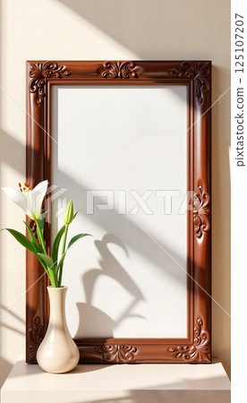 Ornate brown frame with intricate carvings stands empty on a surface, casting a shadow. A delicate white lily with green buds is in a simple beige vase next to it 125107207