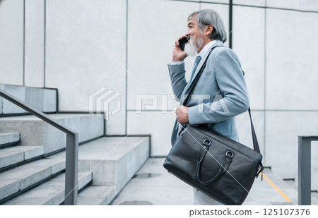 Phone call, communication and mature businessman talking, networking and planning on a phone walking to work. Smile, corporate and manager speaking on a mobile on a walk on stairs in the city Phone call, communication and mature businessman talking, networking and planning on a phone walking to work. Smile, corporate and manager speaking on a mobile on a walk on stairs in the city 125107376