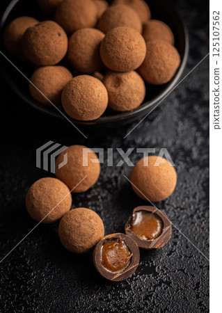 Chocolate truffles with cocoa powder and caramel filling on black table. 125107562
